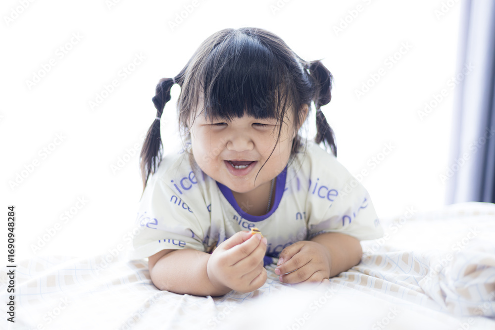 Fototapeta premium A cute little Asian girl is smiling happily on the bed,Newborn baby girl laughing happily, cute smile of little asian child and childhood concept.