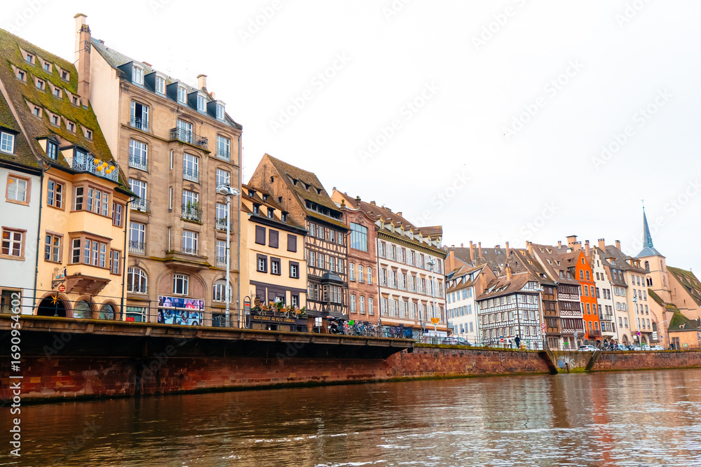Naklejka premium Enjoy a beautiful view of Colmar's historic buildings adorned for Christmas along the tranquil river. The festive spirit brings warmth to the city's picturesque scenery.