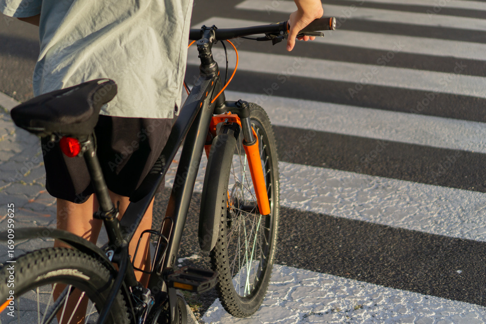 Fototapeta premium Boy on a bicycle looking away from the camera, standing at a pedestrian crossing, a concept of urban life, safety, and a healthy lifestyle.