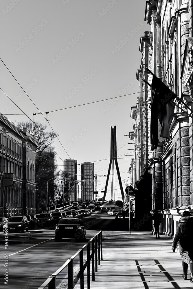 Obraz premium A black-and-white, realistic photograph of a cityscape featuring a bridge. The image emphasizes architectural details, lines, and contrasts, creating a timeless and dramatic urban atmosphere.