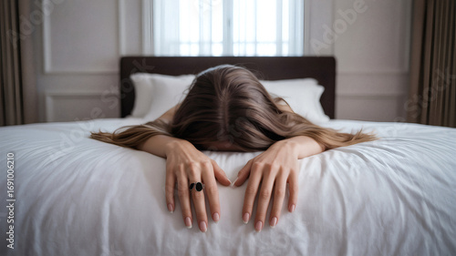 Woman Lying Face Down on White Bed with Brown Hair and Black Ring