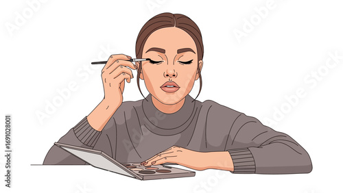 Young woman applying eye makeup with a brush while looking at her reflection in an open laptop computer screen