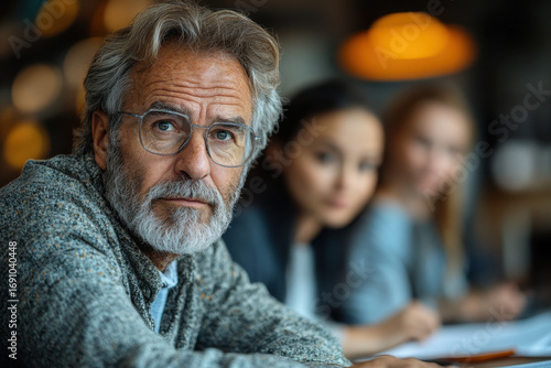 Older man with glasses and grey beard sitting at table with young girls.