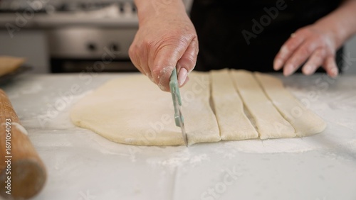 Baker cutting dough into strips in kitchen