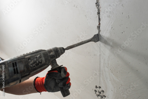 Closeup of worker hand with hammer drill while drilling wall - electrical wiring installation and chasing