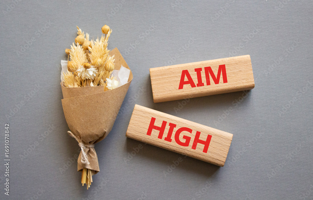Aim High symbol. Wooden blocks with words Aim High. Beautiful grey background with bouquet of flowers. Business and Aim High concept. Copy space.