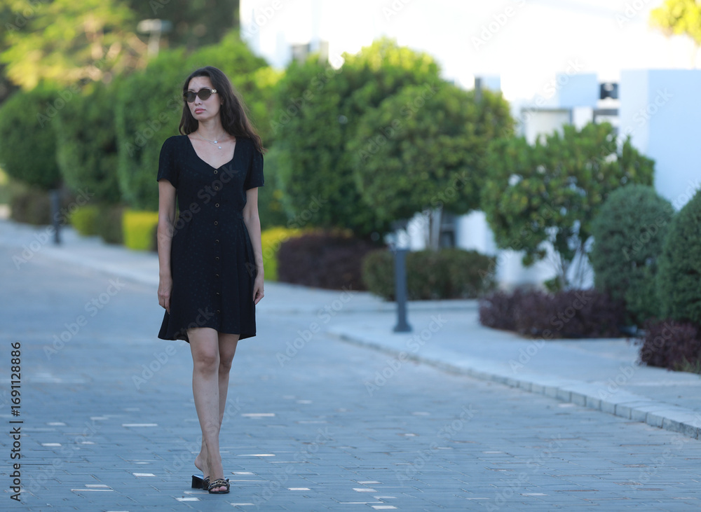 Fototapeta premium portrait of tall slim brunette woman in black fashionable short dress at resort