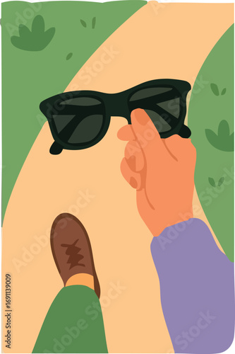 person walking on a path holding black sunglasses, with one brown shoe and green pants visible.