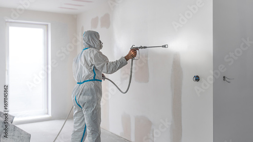 Spray painting walls. Painter wearing protective overalls while painting interior walls with a sprayer.