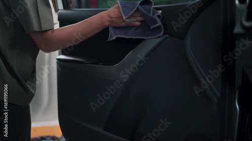A close-up view of a thorough car interior cleaning shows a hand diligently wiping the inside of the car door with a microfiber cloth emphasizing the meticulous attention to detail of the car.