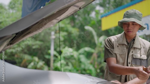 A person stands beside a car with the hood up, looking for help with an anxious look in his eyes.