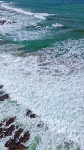 Vertical 4K Drone Video of Ocean Waves Crashing on Rocky Coastline. Vertical aerial drone footage of ocean waves crashing on rocky coast with white foam.