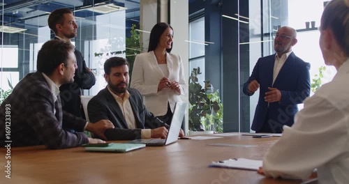 Senior leader talking on business training and briefing meeting, speaker explaining strategy presentation to project team in modern glass office. Colleagues listening speech at boardroom table