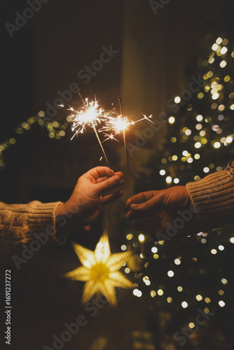 Happy New Year! Burning sparklers in hands on background of christmas tree golden lights bokeh at night. Glowing fireworks in couple hands, new year eve holiday celebration
