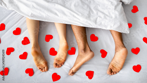 Valokuva Top view of millennial interracial couple resting after making love on bed, surrounded by red paper hearts