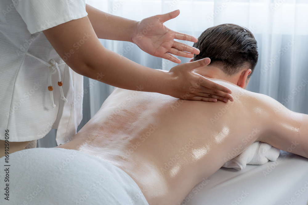 Obraz premium Caucasian man customer enjoying relaxing anti-stress spa massage and pampering with beauty skin recreation leisure in day light ambient salon spa at luxury resort or hotel. Quiescent