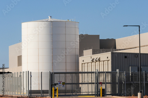 Cylindrical storage tank positioned outside a large data center campus with perimeter fencing and industrial infrastructure supporting cloud computing and technology operations