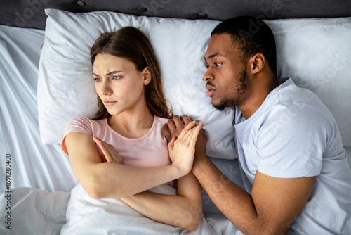 Sexual apathy concept. African American guy touching his upset girlfriend in bed, woman refusing him, top view. Young black couple having difficulties in sex, suffering from relationship problems