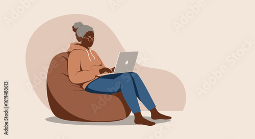 Comfortable senior Black woman using a laptop on a bean bag chair. Represents remote work, online learning, and digital lifestyle for older adults.