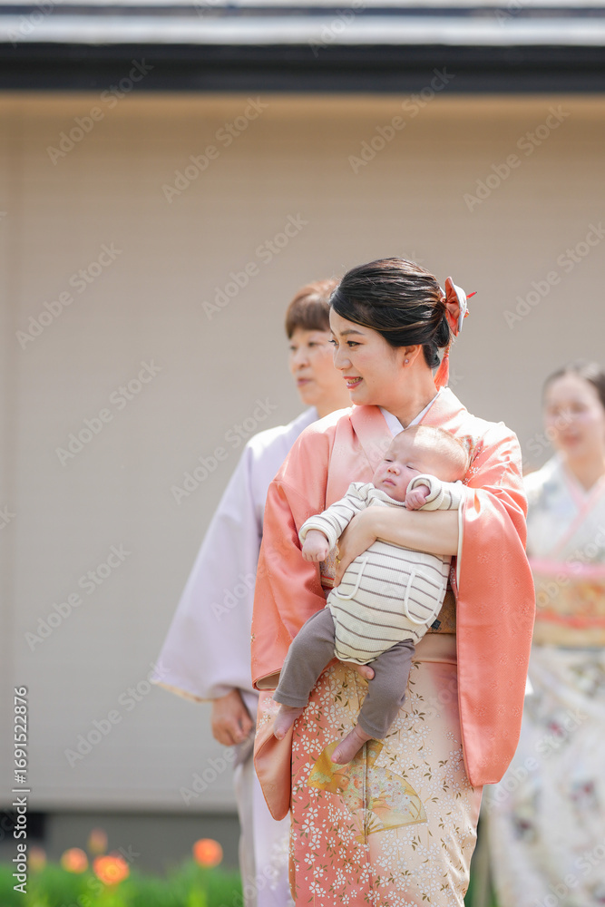 Obraz premium A woman in a pink kimono is holding a baby. The baby is sleeping and the woman is smiling. The scene is peaceful and heartwarming