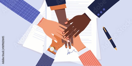 Diverse team of people stacking hands together over documents with a pen nearby symbolizing unity and collaboration