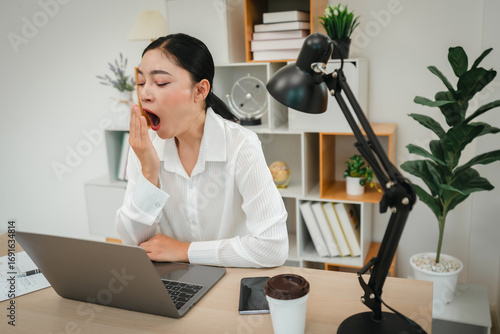 sleepy woman yawning while working with laptop computer at home office