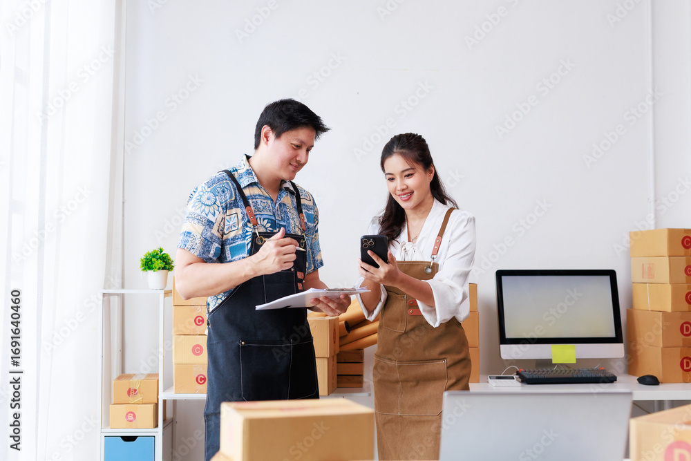© amnaj - Two people working in a warehouse with cardboard boxes and a computer, managing online orders with a smartphone and a clipboard © amnaj - Two people working in a warehouse with cardboard boxes and a computer, managing online orders with a smartphone and a clipboard