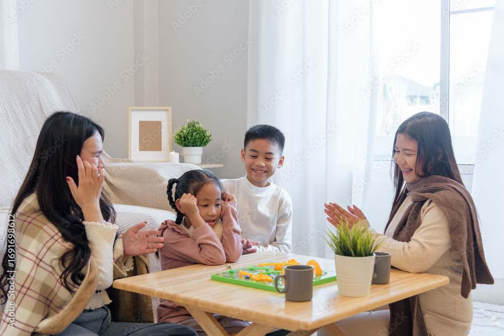 Fototapeta premium During winter, a family enjoys time together indoors playing a board game at a small table, creating a warm and happy moment, as they celebrate a fun winter day together