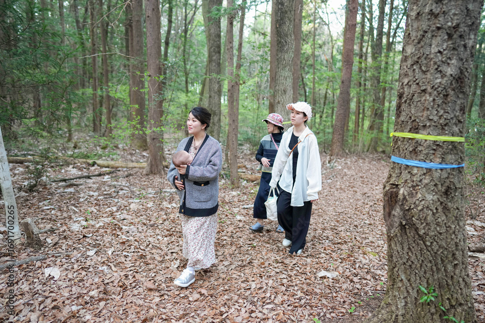Fototapeta premium A group of people are walking through a forest, one of them holding a baby. Scene is peaceful and serene, as the group seems to be enjoying their time in nature