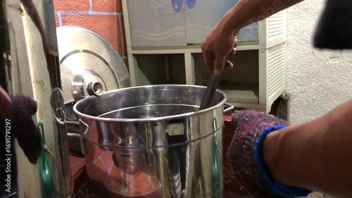Asian man scalds a wine bottle in boiling water to pasteurize it, then places it on a wooden rack while  working in a small local winery.