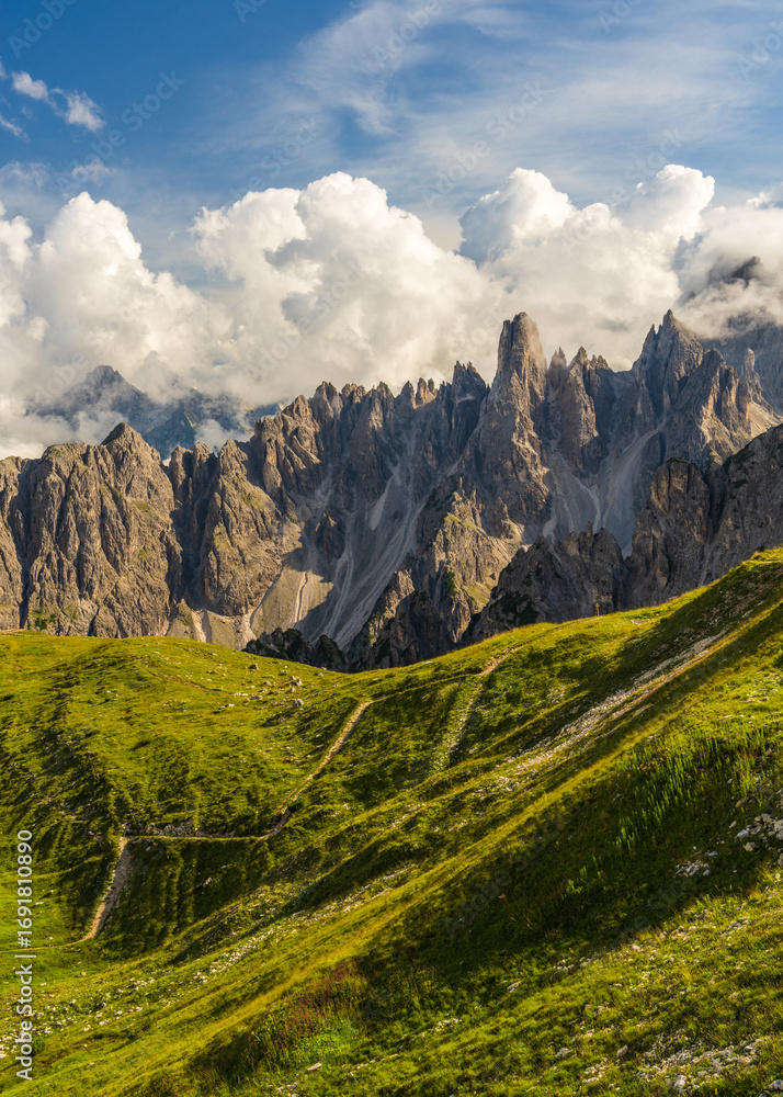 Fototapeta premium Stunning vertical shot of Dolomites featuring dramatic rocky peaks, lush alpine meadows, clear blue sky. Classic mountain landscape of northern Italy, perfect for travel, outdoor themes.
