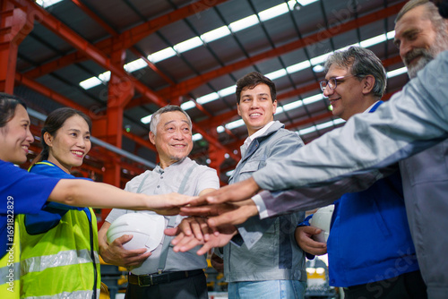 Engineers and workers in factory raising hands together, showing teamwork and unity.