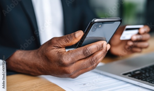 Close-up of dark-skinned hands holding a phone and credit card, likely making a mobile payment