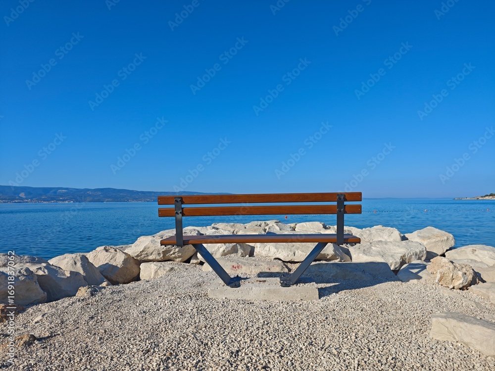Obraz premium Peaceful bench overlooking calm waters at a coastal location on a bright, sunny day