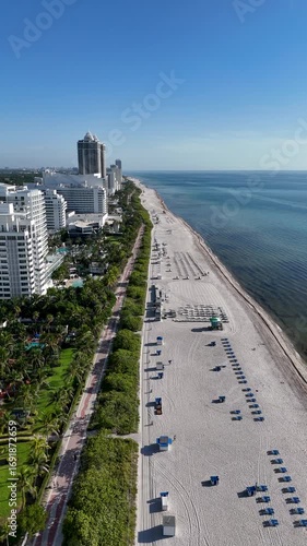Vertical 4K aerial drone video of Miami Beach, Florida, showing the long sandy coastline, turquoise Atlantic Ocean, palm-lined promenade, and skyline of luxury hotels on a clear sunny day, perfect for