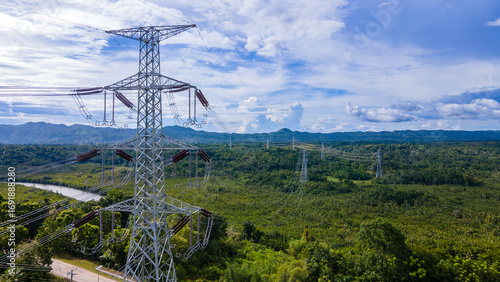 Electricity transmission towers crossing a green forest with mountains and blue sky. Energy and infrastructure concept