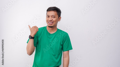 Young Asian man smiling when looking and pointing to the left side on white background.