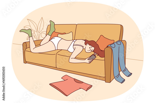 Lazy woman in underwear lies on sofa and uses phone, not paying attention to chaos in apartment. Scattered things around lazy girl who suffers from procrastination and does not want to clean room.