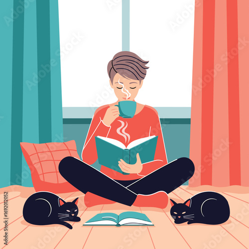 A person enjoys a warm drink while reading a book with two cats nearby