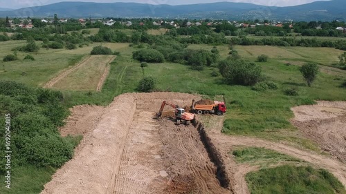 Aerial footage of an excavator loading soil into a dump truck on a dirt construction site.