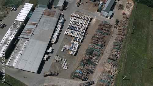 This aerial footage captures the full layout of a timber processing facility from above, showcasing lumber storage, production buildings, and surrounding road infrastructure