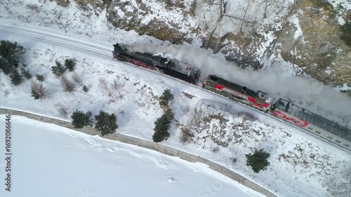 Aerial view of incredible authentic steam locomotive releasing smoke from chimney on snowy winter railway Unique vintage train journey through breathtaking frozen landscape, majestic winter scenery 4k
