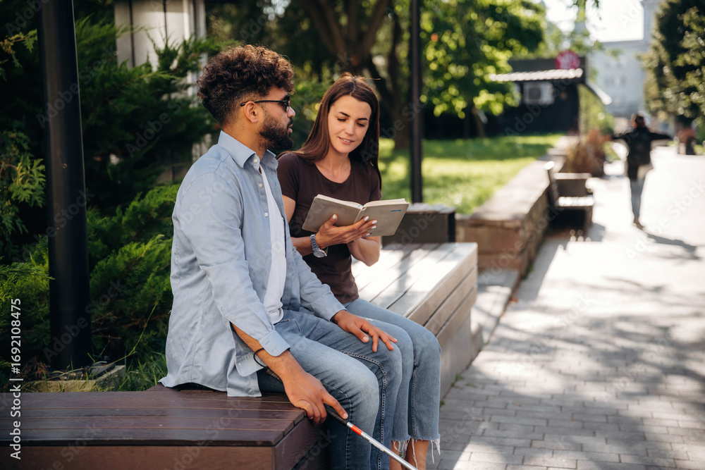 Fototapeta premium Woman is with blind man, sitting outdoors and reading book