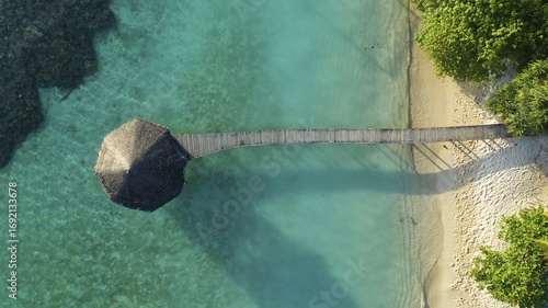 Aerial view of a rustic wooden pier stretching into the turquoise waters, contrasting sharply with the pristine white sands of the beach, Maldives.