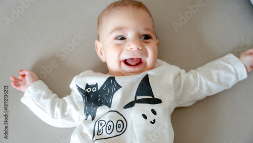 Baby in halloween themed outfit lying on gray background