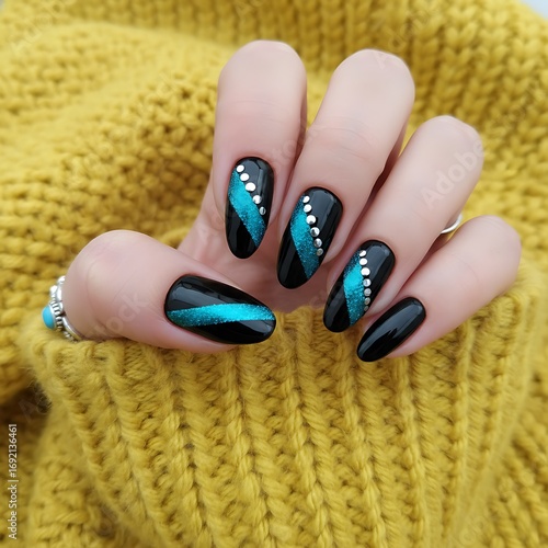 Close up of a woman s hand with stunning black and teal cat eye nail art adorned with sparkling rhinestones against a cozy yellow knitted sweater
