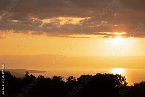 Coucher de soleil sur le lac Léman or brillant dans un ciel de nuages sombres avec vue sur sur la silhouette de la rive suisse. 