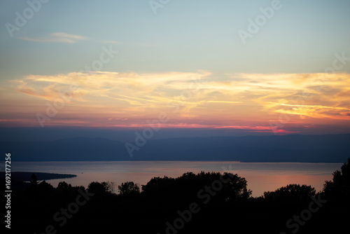Coucher de soleil sur le lac Léman orange brillant dans un ciel de nuages en feu rouge et jaune avec vue sur sur la silhouette de la rive suisse. 