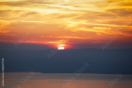 Coucher de soleil sur le lac Léman or brillant dans un ciel de nuages en feu rouge et jaune avec vue sur sur la silhouette de la rive suisse. 