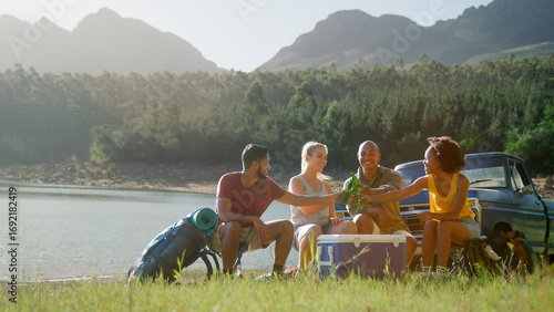 Group Of Friends With Backpacks By Pick Up Truck On Road Trip Drinking Beer From Cooler By Lake